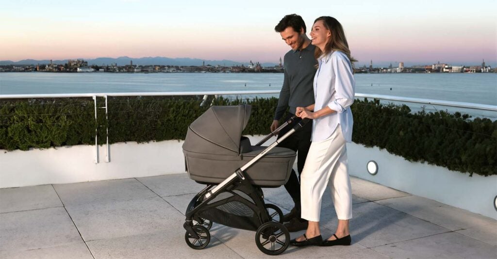 Parents poussant la poussette Inglesina Aptica au bord de l'eau au coucher du soleil, poussette combinée élégante et polyvalente pour bébé