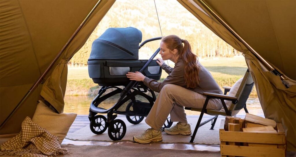 Maman avec sa poussette Inglesina Aptica XT dans un tipi face à un lac, poussette tout terrain adaptée aux aventures en plein air avec bébé