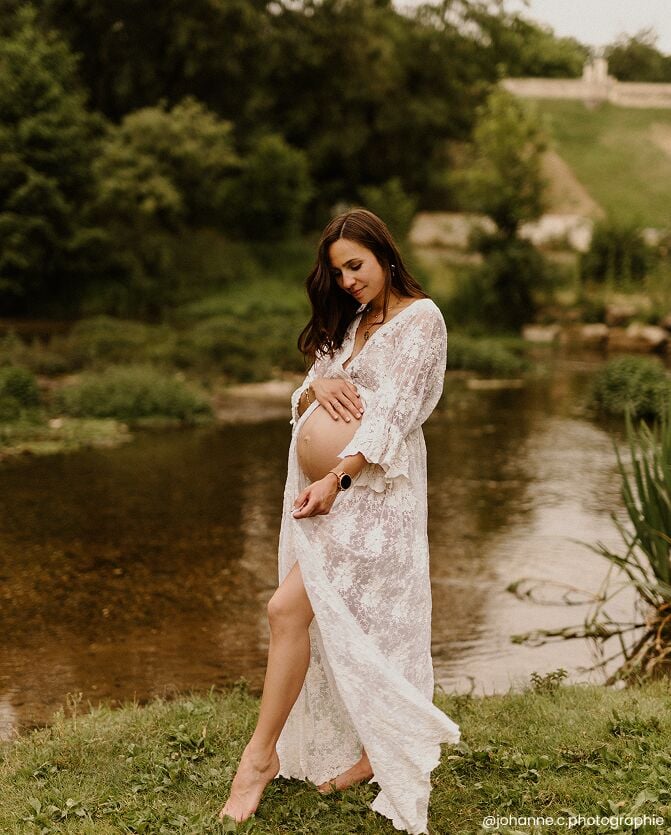 Manon enceinte en robe blanche près d'un cours d'eau, portrait de future maman, séance photo de grossesse en pleine nature