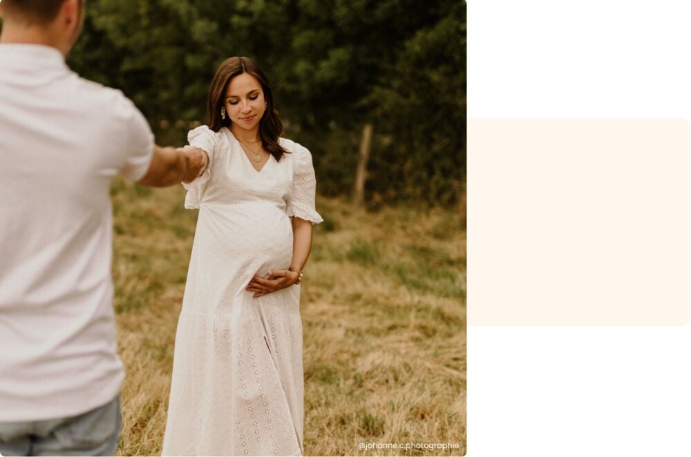 Manon enceinte main dans la main avec son compagnon dans un champ, préparation à la maternité, couple attendant leur premier bébé