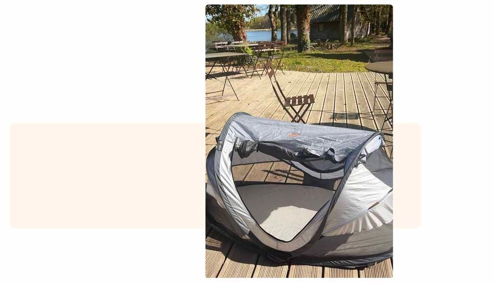 Lit de voyage pop-up bébé installé sur une terrasse en bois face à un lac, checklist camping bébé, lit portable indispensable pour faire dormir bébé en extérieur