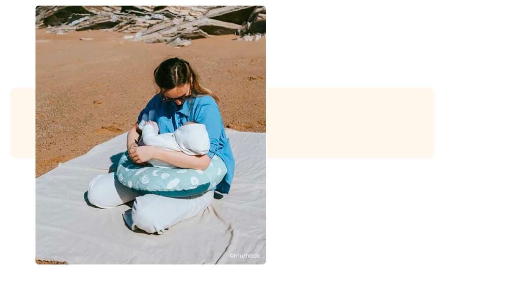 Maman allaitant son nouveau-né sur une plage avec coussin d'allaitement, conseils pour partir camper avec un bébé, allaitement et confort en plein air