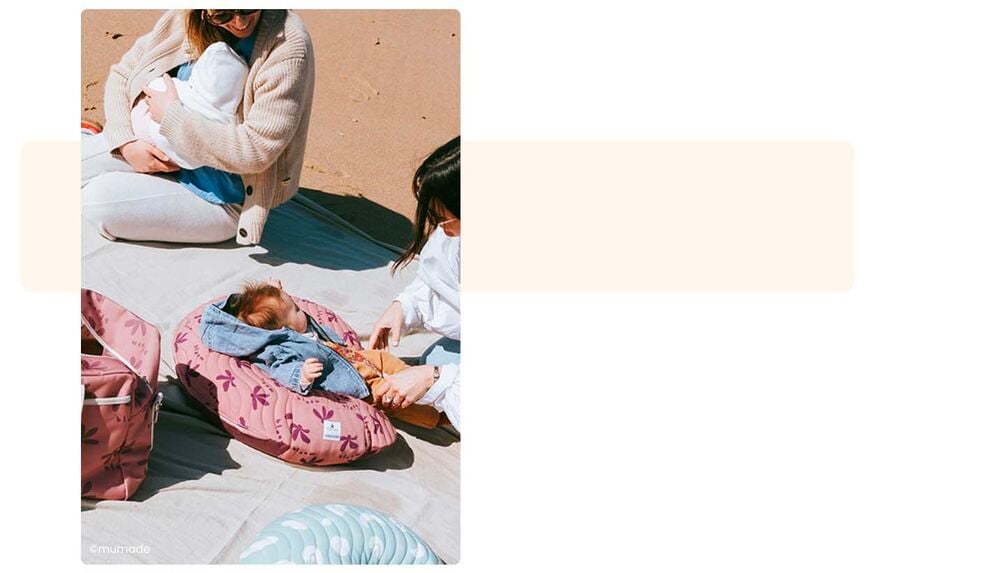 Maman allaitant et bébé installé sur un coussin d'allaitement sur la plage, produits soin et hygiène bébé camping, indispensables à glisser dans le sac