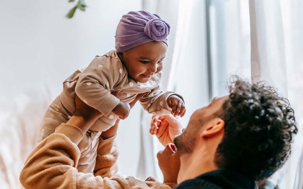 Préparer arrivée enfant adopté, accueillir les premiers jour. Renforcer le lien parent-enfant : Un père souriant tenant son bébé adopté dans les airs, partageant un moment de complicité. Informations et soutien pour les parents adoptifs dans le parcours de l'adoption.