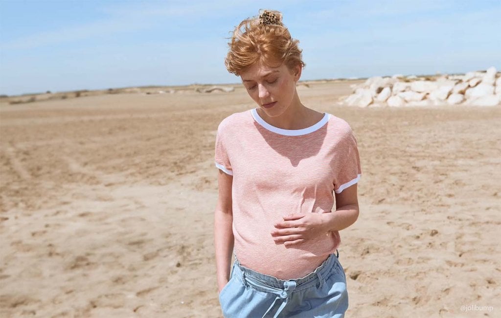 Femme enceinte touchant doucement son ventre sur une plage, pensant à son inscription en maternité, vue rapprochée pour illustrer le processus de choix et d'inscription à la maternité, guide pratique pour futures mères.