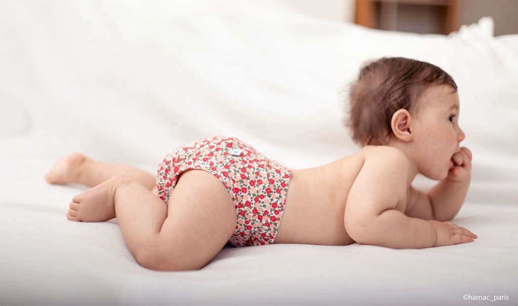 Bébé allongé sur le ventre portant une couche lavable à motifs fleuris, alternative écologique et confortable aux couches jetables