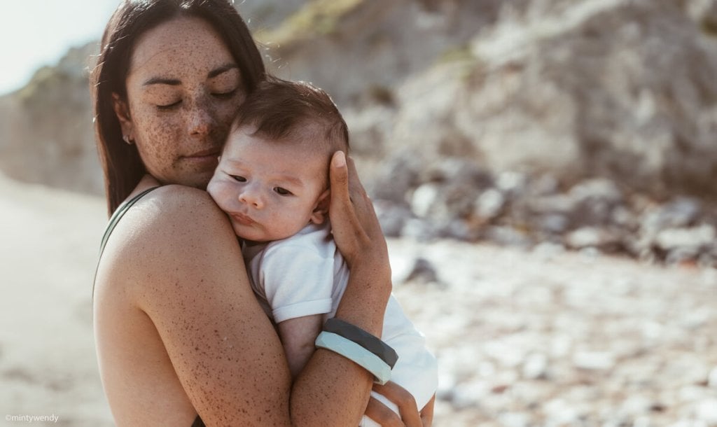 Mère tenant son nourrisson contre elle sur une plage, connexion peau à peau et douceur, représentation de la transformation maternelle