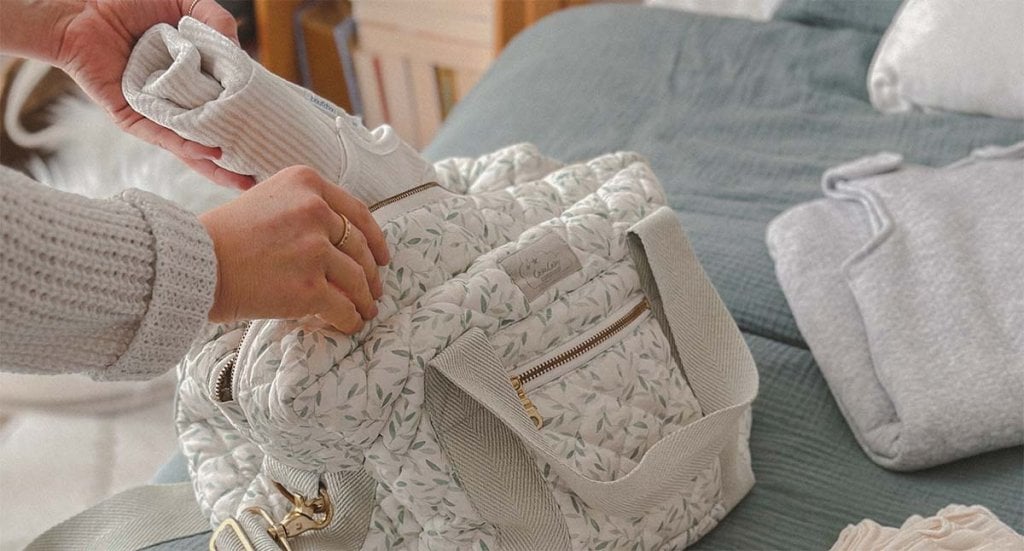 Valise de maternité fleurie en cours de préparation avec vêtements de bébé soigneusement rangés