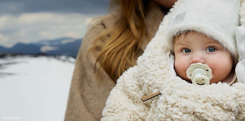 Vacances neige avec bébé : nourrisson emmitouflé dans un équipement bébé neige chaud, bonnet et couverture douce.