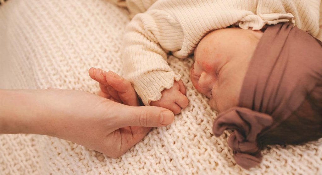 Gros plan tendre d’un nouveau-né agrippant le doigt d’un adulte, évoquant la période suivant un congé maternité