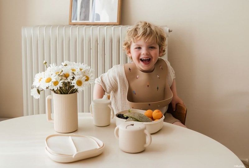 Une petit garçon souriant à une table à côté d'un bouquet de fleurs, évoquant la douceur et l'originalité pour inspirer le choix d'un prénom rare et cool pour un garçon. Liste de prénoms.