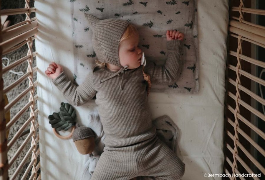 Bébé dormant paisiblement dans un berceau en bois, vêtu d'une confortable combinaison. Cette image sereine illustre l'application réussie de la méthode 'chrono-dodo' pour faciliter les routines de coucher des bébés.