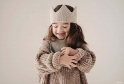 Une petite fille souriante avec une couronne tricotée, évoquant la douceur et l'originalité pour inspirer le choix d'un prénom rare et cool pour une fille. Liste de prénoms.
